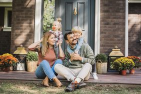 A stock image of a couple with two children in front of a home. 