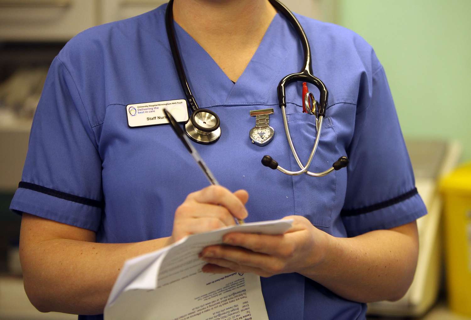 Nurse wearing blue scrubs takes notes. 