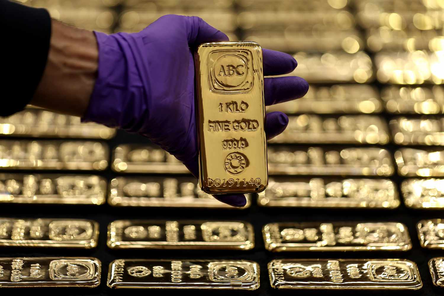 A hand with a purple glove holds 1 kilogram of fine gold