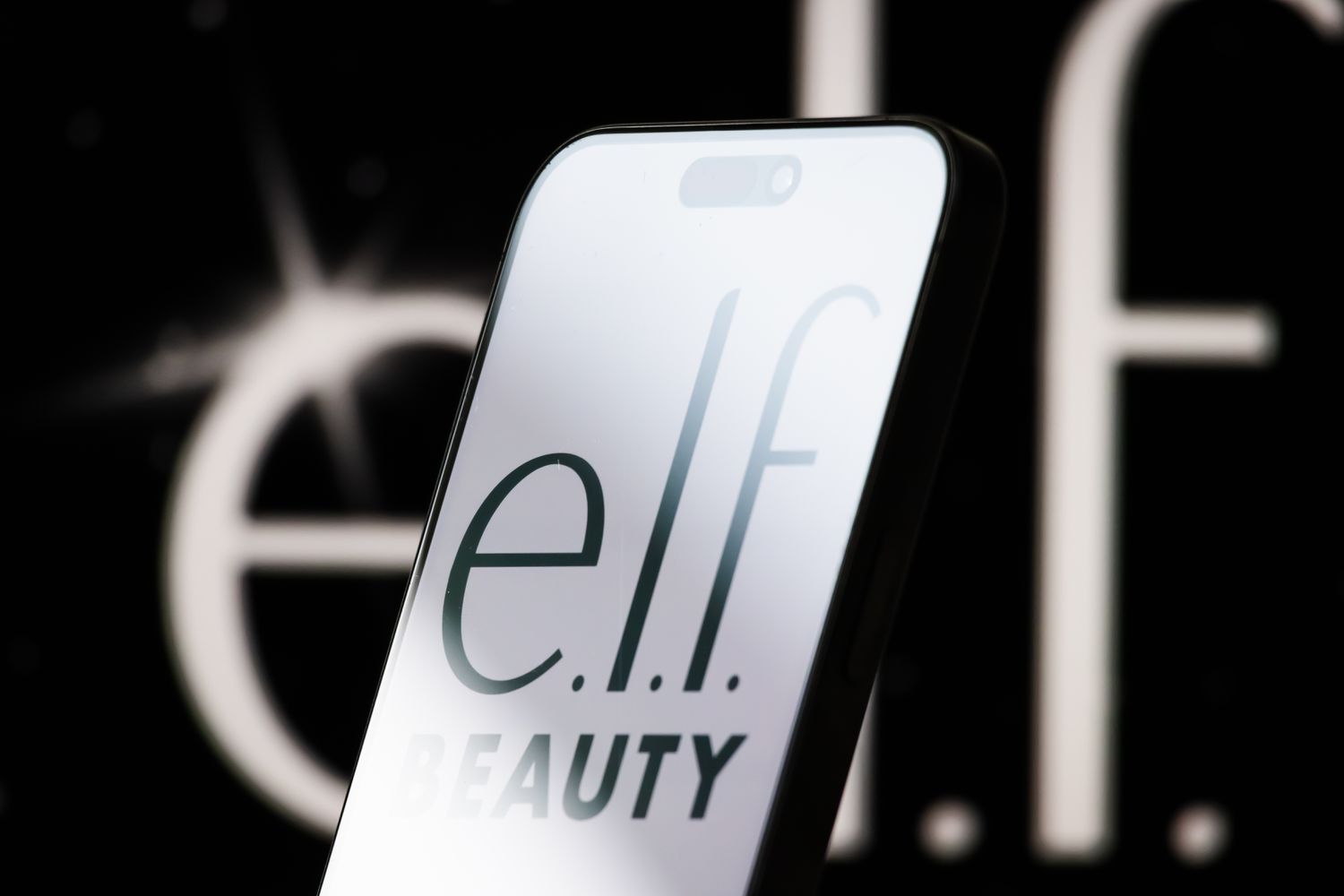 The logo of e.l.f. Beauty is displayed on a smartphone screen, with the company's sleek black-and-white branding visible in the background