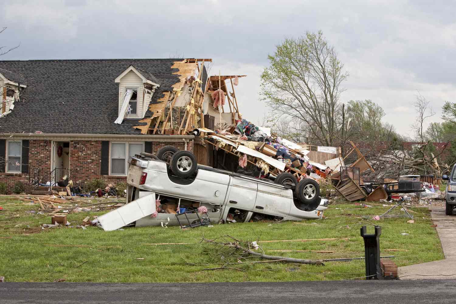 A home damaged by a tornado and an upside down truck in a yard.