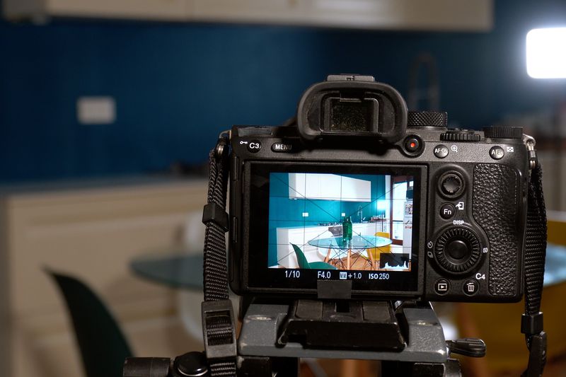 A camera on a tripod capturing a modern kitchen setup seen on its display screen, perspective from behind the camera.