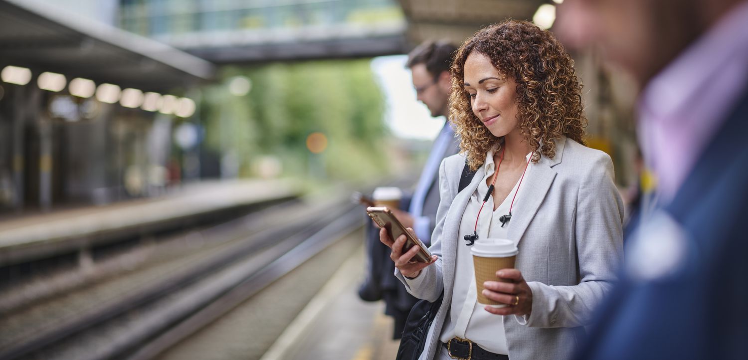 Woman on an outdoor train platform looking at her phone. 