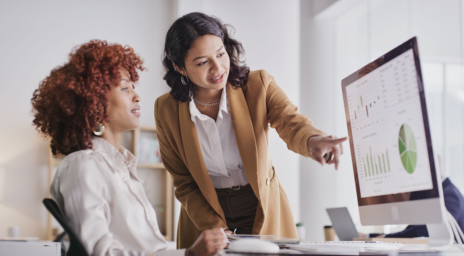 Two women looking at graphs and other data on a computer