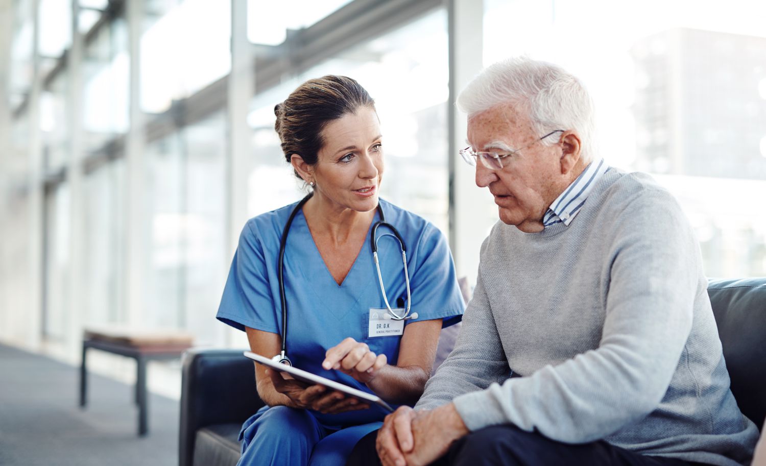 Doctor talking to older patient and showing him something on a tablet computer 