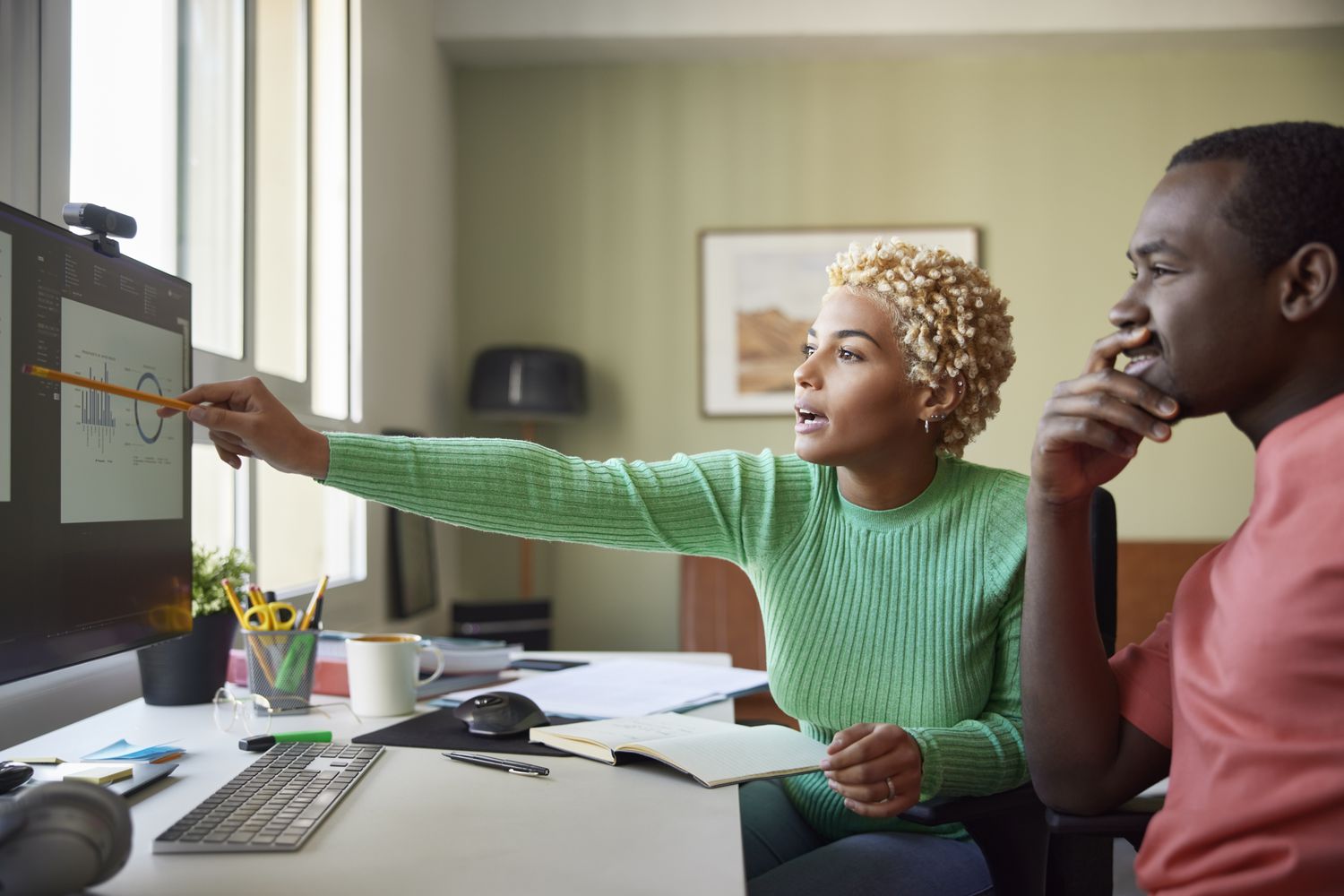Woman sitting by a man points to graphs on a monitor