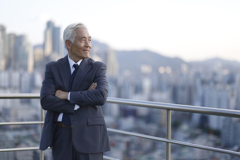 Senior Businessman Standing with Arms Crossed on Rooftop with City Skyline Behind Him