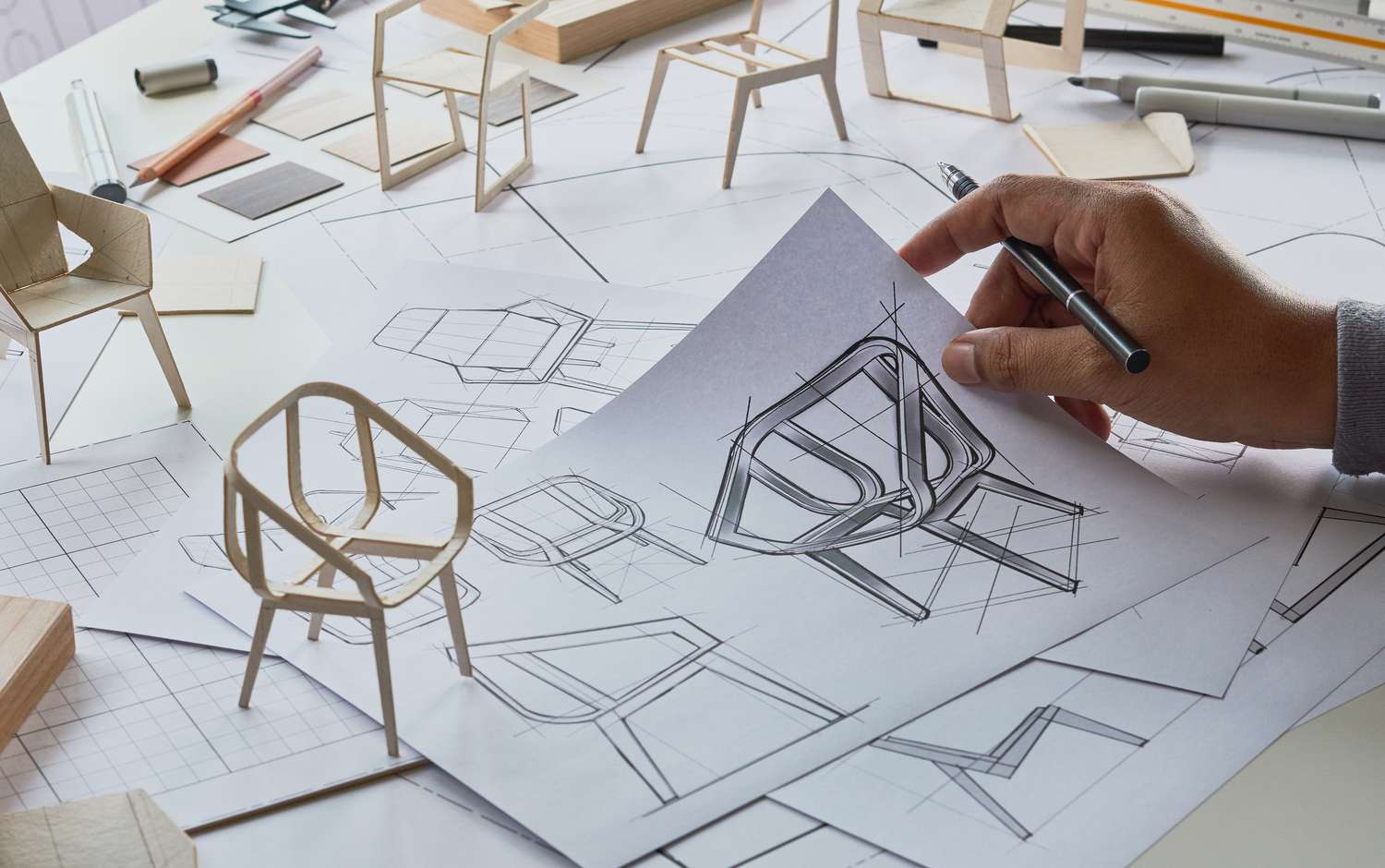 A product designer works with a draft of a armchair and a small model of the chair to refine the final design.