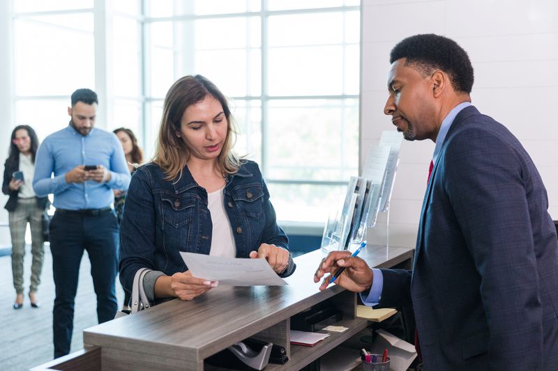A male bank manager talks to a woman at the bank counter.