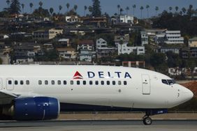 A Delta Air Lines plane is seen on the runway at San Diego International Airport, with houses in the background..