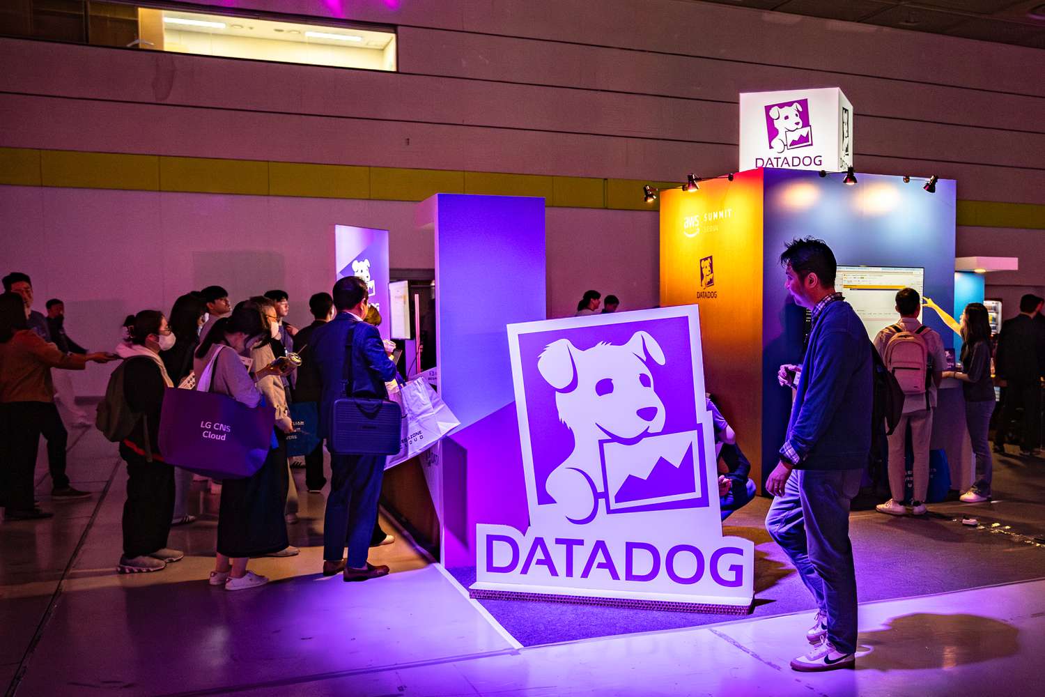 People walk by the purple Datadog logo on the floor of a conference center.