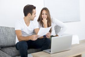 Young couple sitting on their sofa and looking together at mortgage rates on a laptop