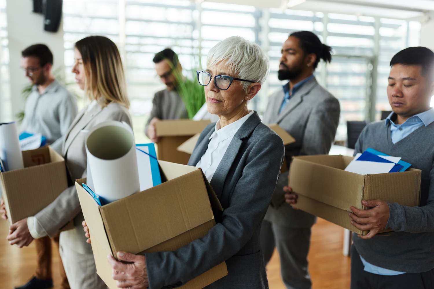 A group of sad employees carry cardboard boxes filled with their office belongings after being laid off due to economy stagnation. 