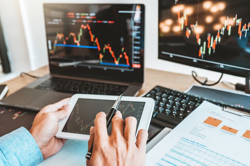 Investor reviews stock market data on tablet and laptop.