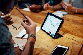 Mixed group of millennial aged friends discuss investing and cryptocurrency trading at a cafe. Depicts TradingView financial market chart.