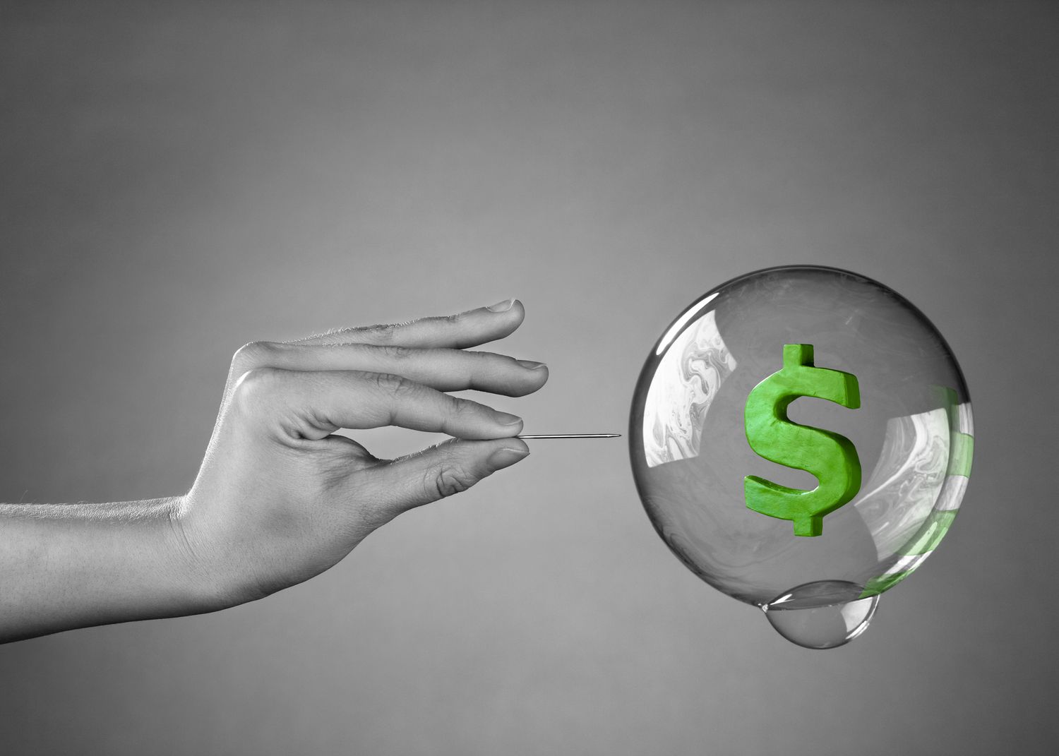 A hand about to burst a money bubble with a pin.