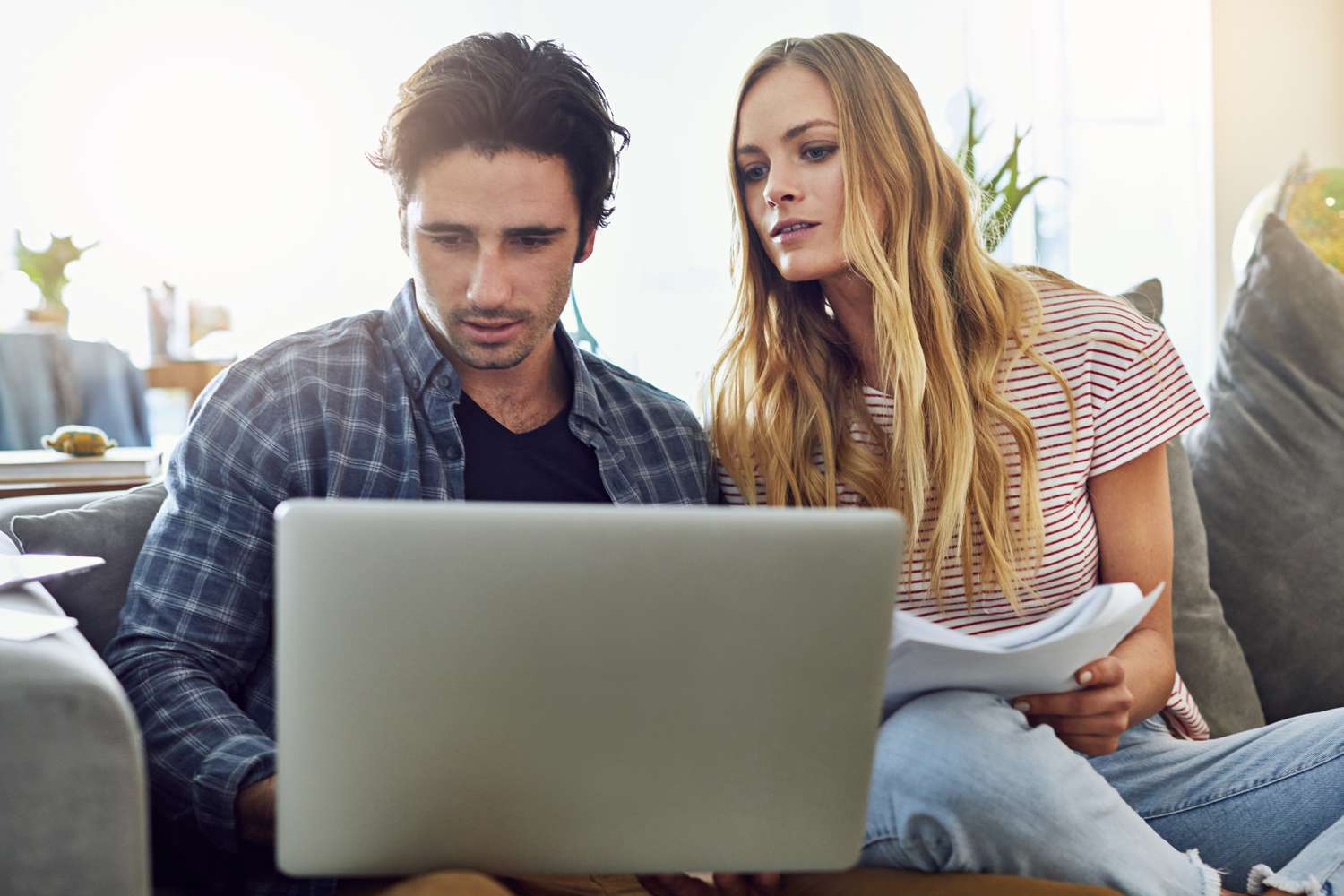Young couple sitting on their couch and looking together at a laptop and documents