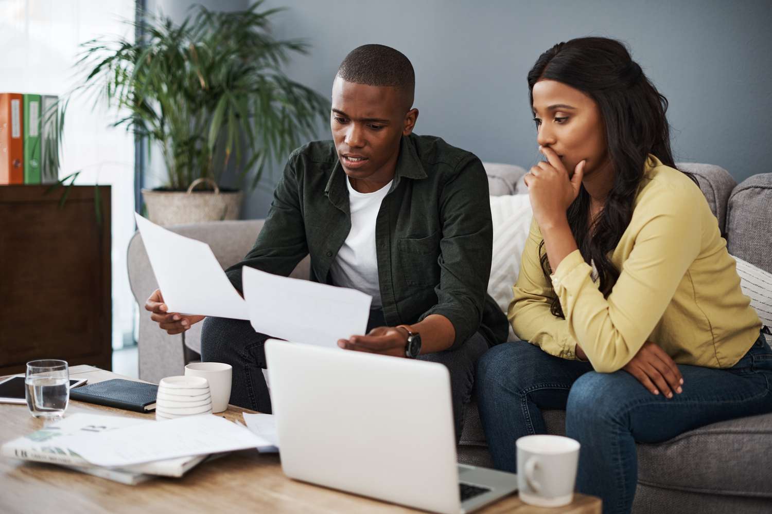 Young couple sitting on their sofa and looking intently at documents and a laptop