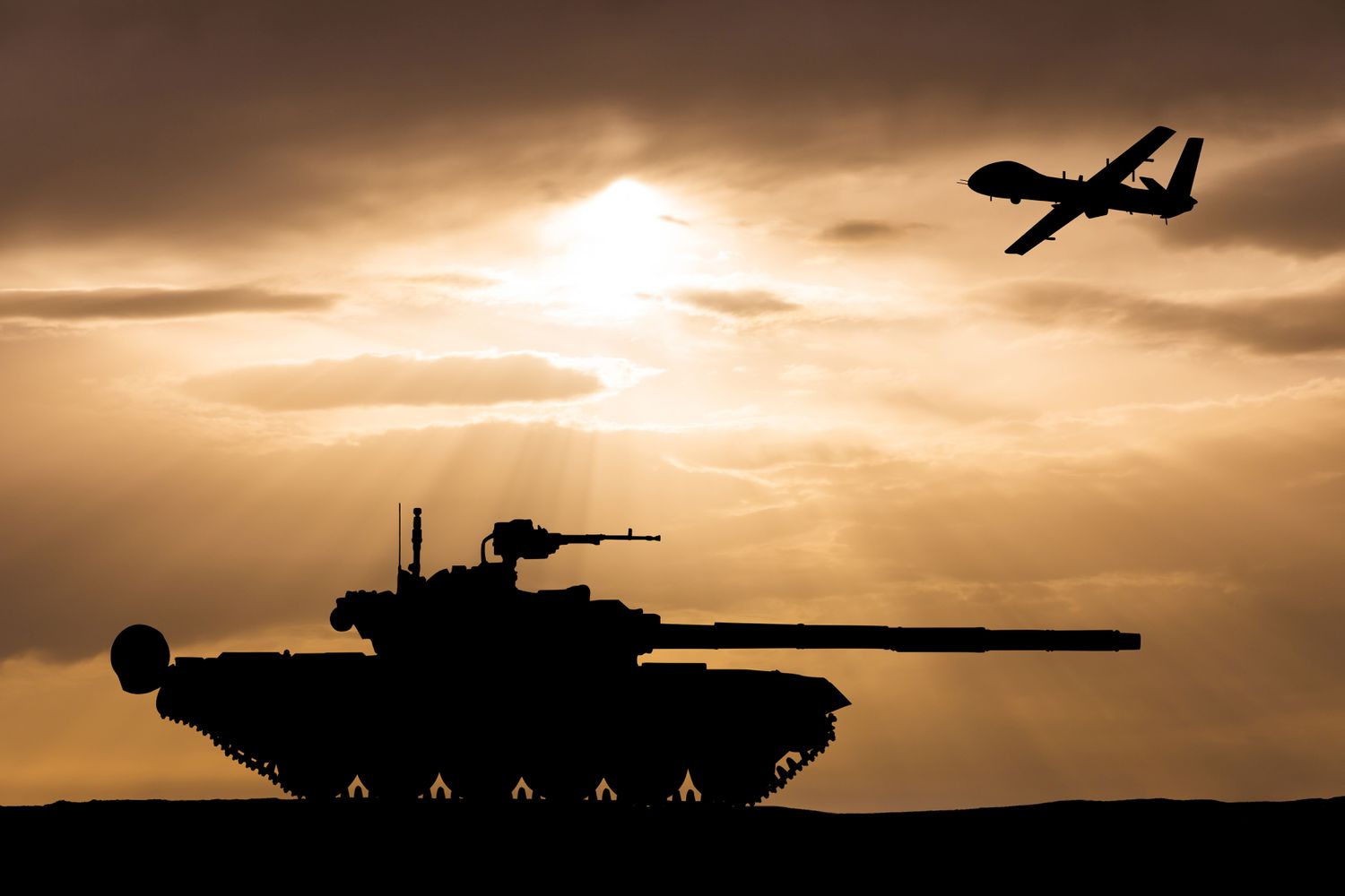 Military tank shown beneath a fighter jet at sunset