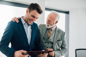Older business man hugging younger coworker