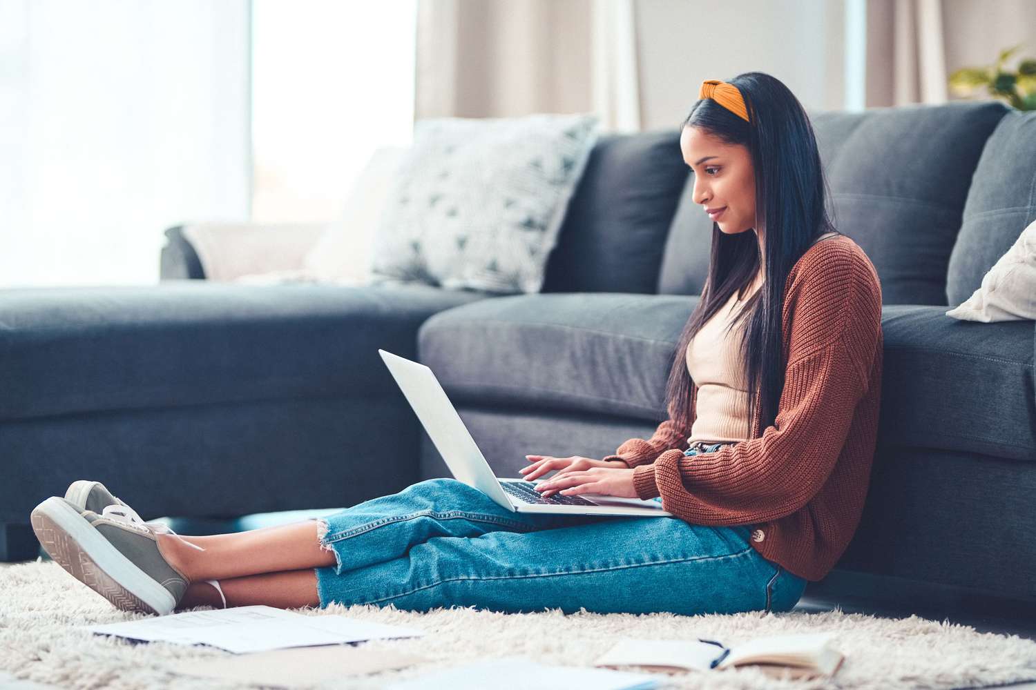 young woman using a laptop while going through student loans paperwork in the living room at home