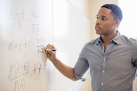Student working out math equation on whiteboard in classroom