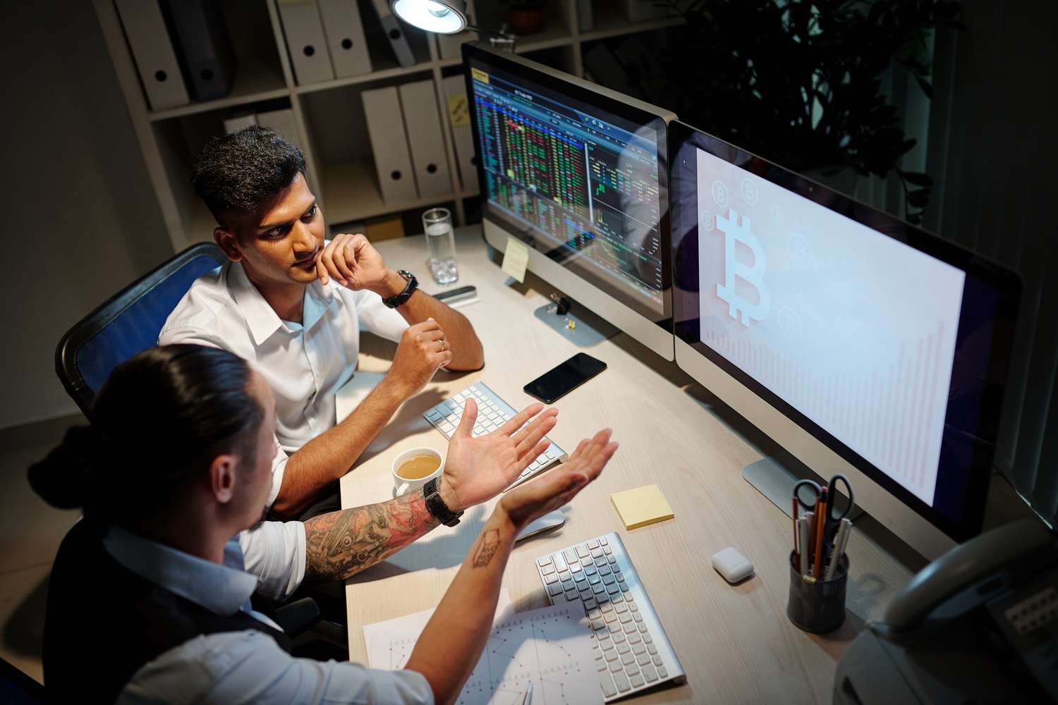 Two people discussing crypto trading while looking at computer screens