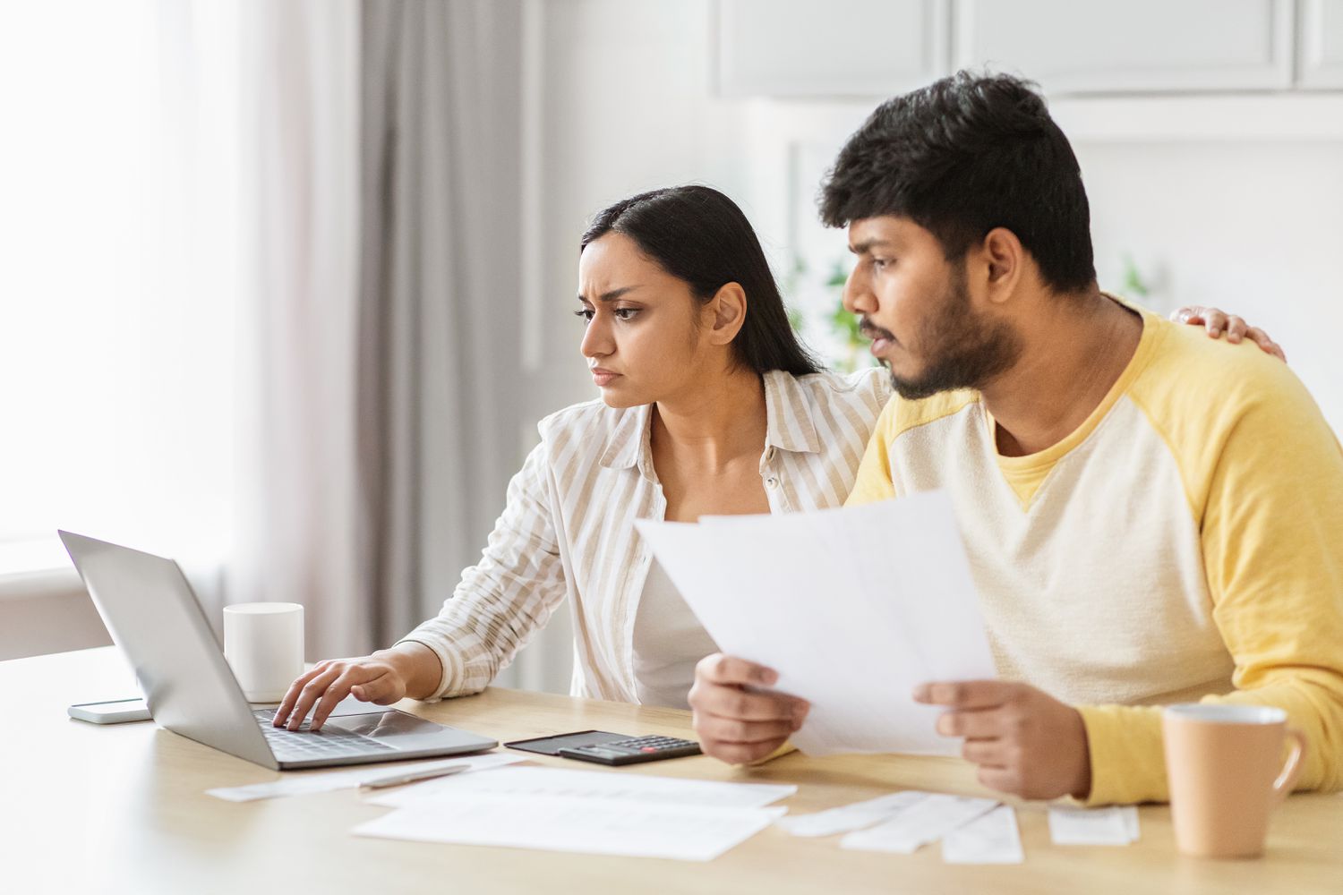 A couple delves into financial planning, one using a computer and the other looking at printed documents