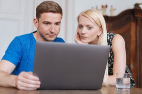 Young couple sitting at their dining room table and looking together at mortgage rates on a laptop