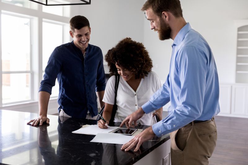 A real estate agent shows new homeowners where to sign on the closing documents. They are standing in an empty home.