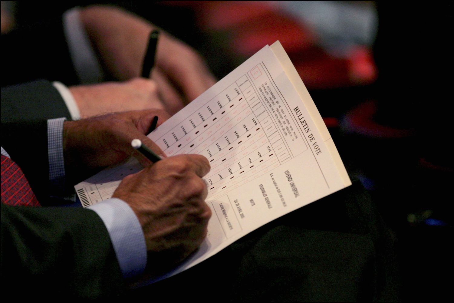 A shareholder uses a pen to fill out a ballot selecting a new board director during a shareholder meeting.
