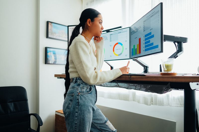 Woman working on a computer at a standing desk. The screens display colorful charts. 