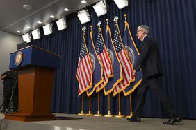 Jerome Powell walks across a stage, toward a podium. Behind him are U.S. and Federal Reserve flags.
