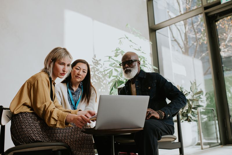 Three people sit round a low table looking at a laptop screen