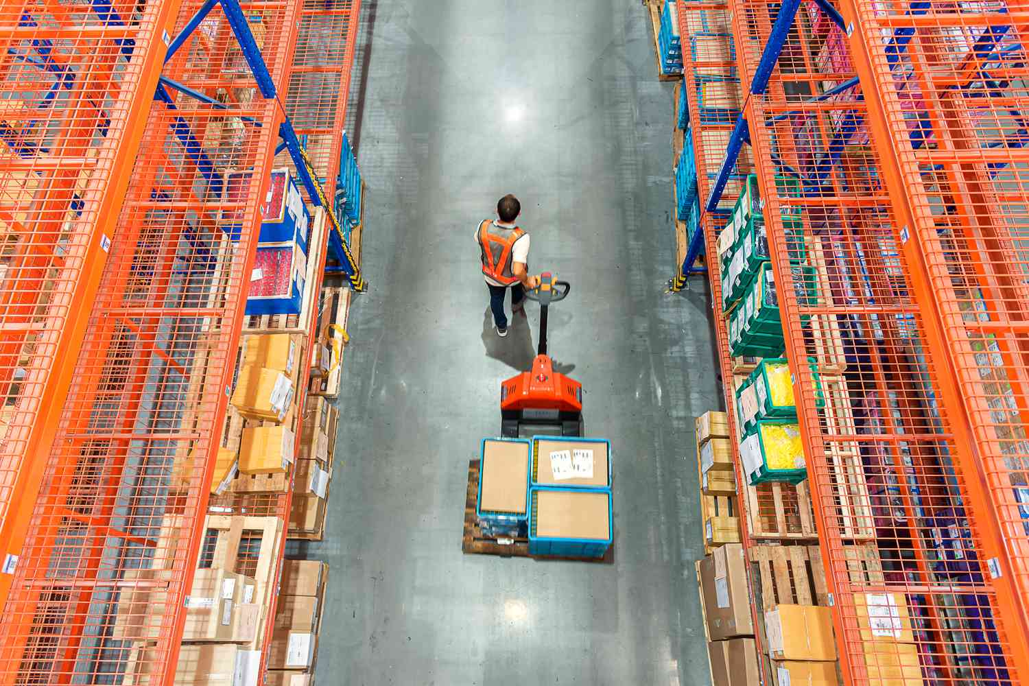 Warehouse worker pulling a pallet truck at distribution warehouse.