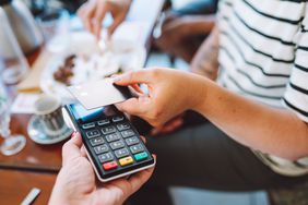 Person tapping their credit card against a card reader while sitting at a restaurant table