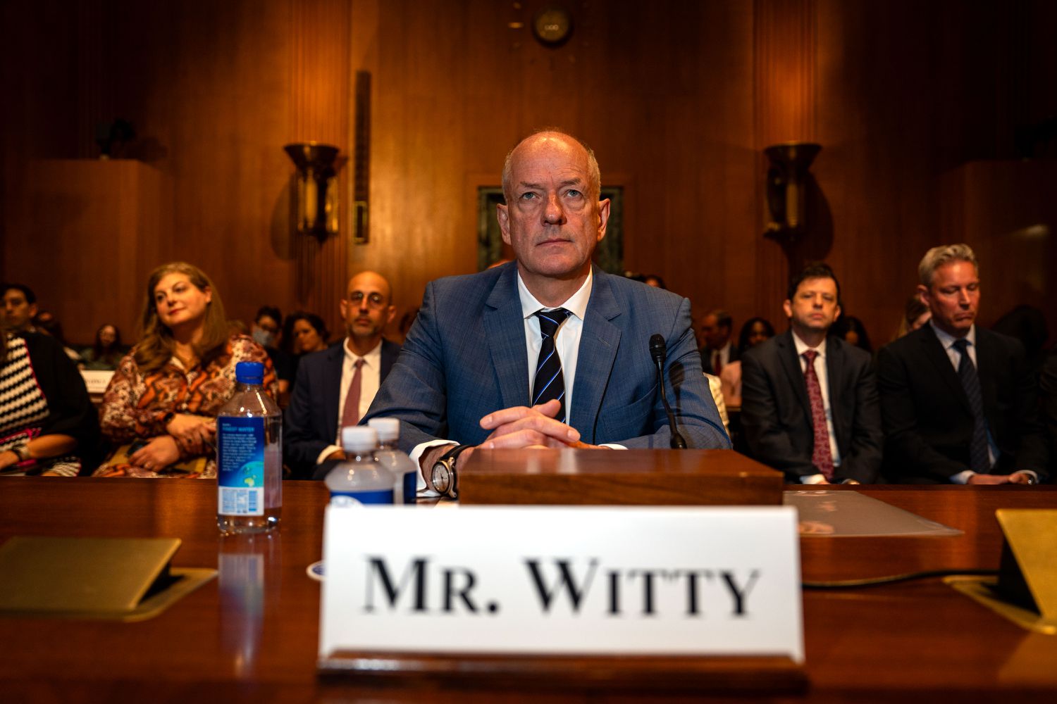 UnitedHealth Group CEO Andrew Witty sits at a table during a Senate hearing, with other people seated behind him.