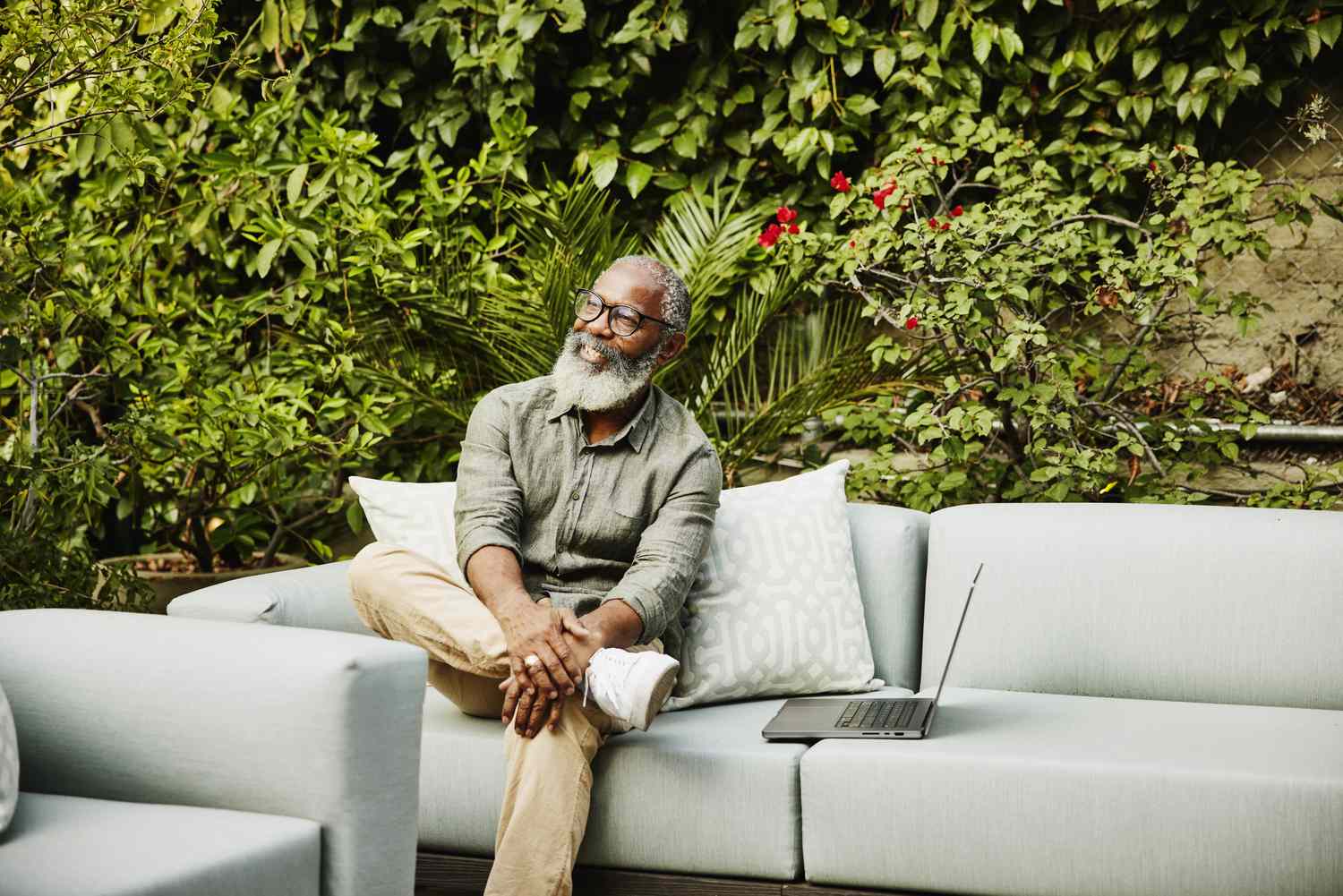 Medium wide shot portrait of smiling senior man with laptop sitting in garden on rooftop deck