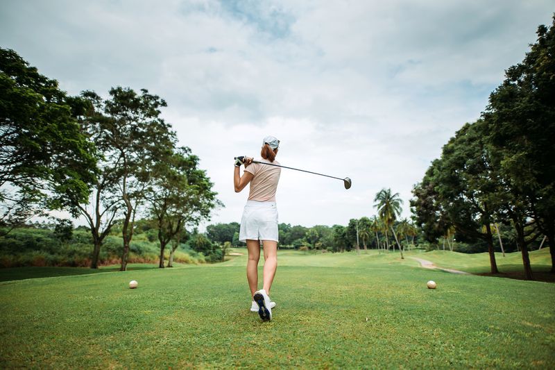 Golfer swinging on a golf course, trees in the background