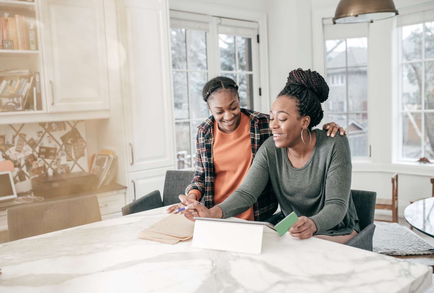 Two women looking at a tablet on a kitchen counter island.