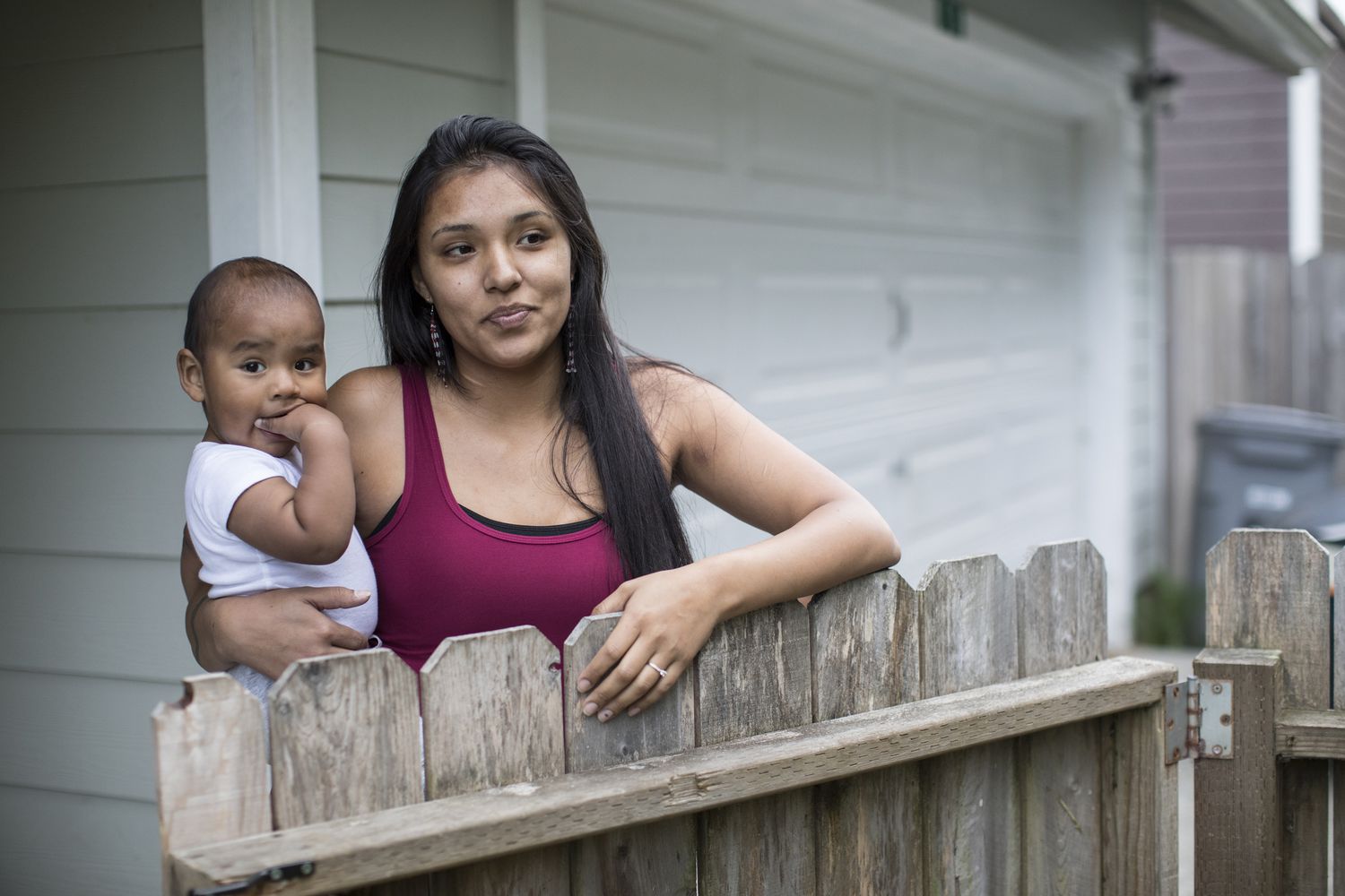 Native American mom holds baby at front gate to their home