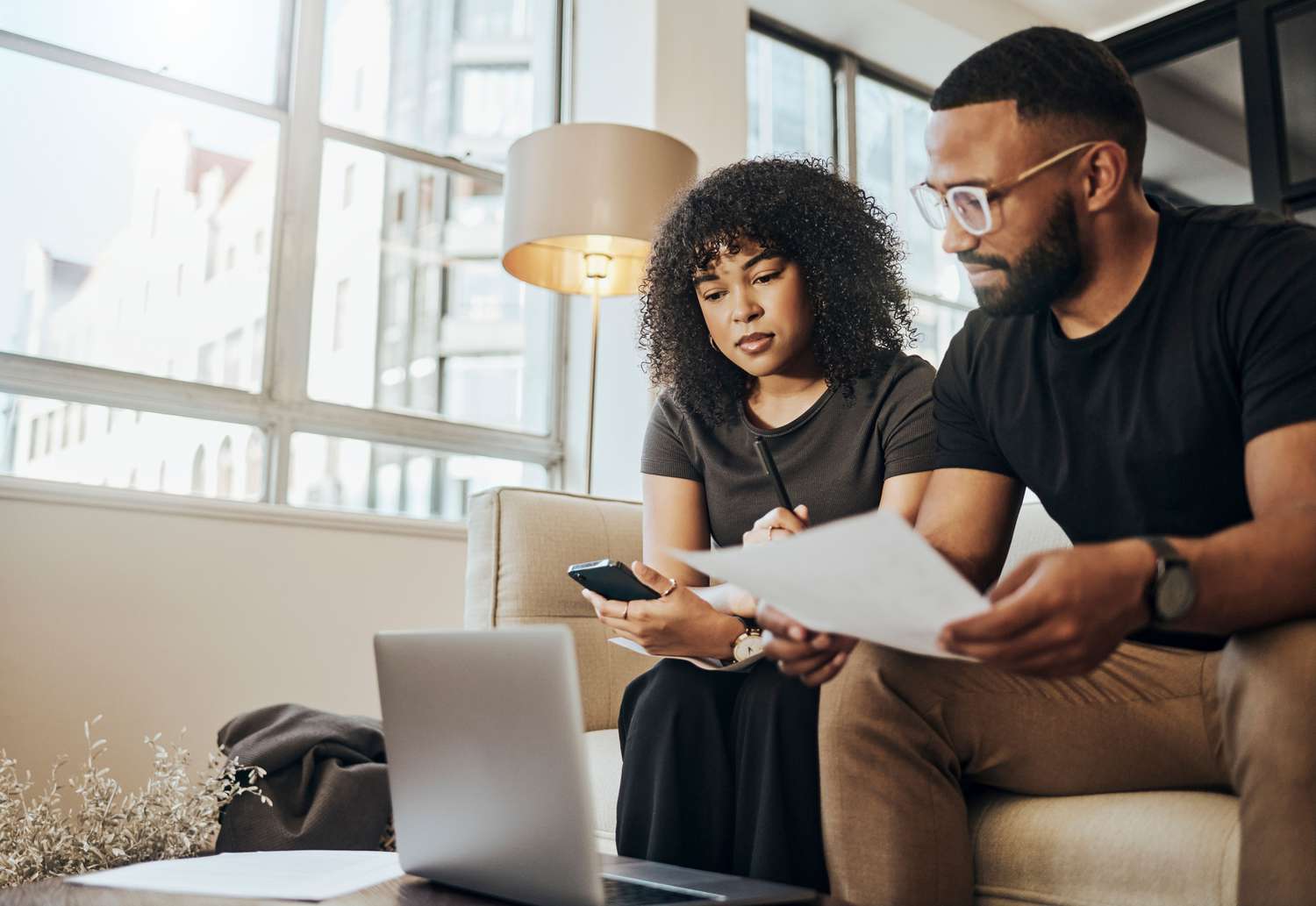 Woman and man looking a paperwork with a laptop on a couch