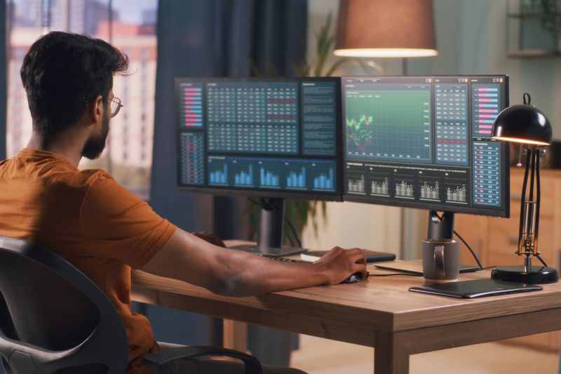 Person seated at a desk, looking at computer monitors showing market trading data