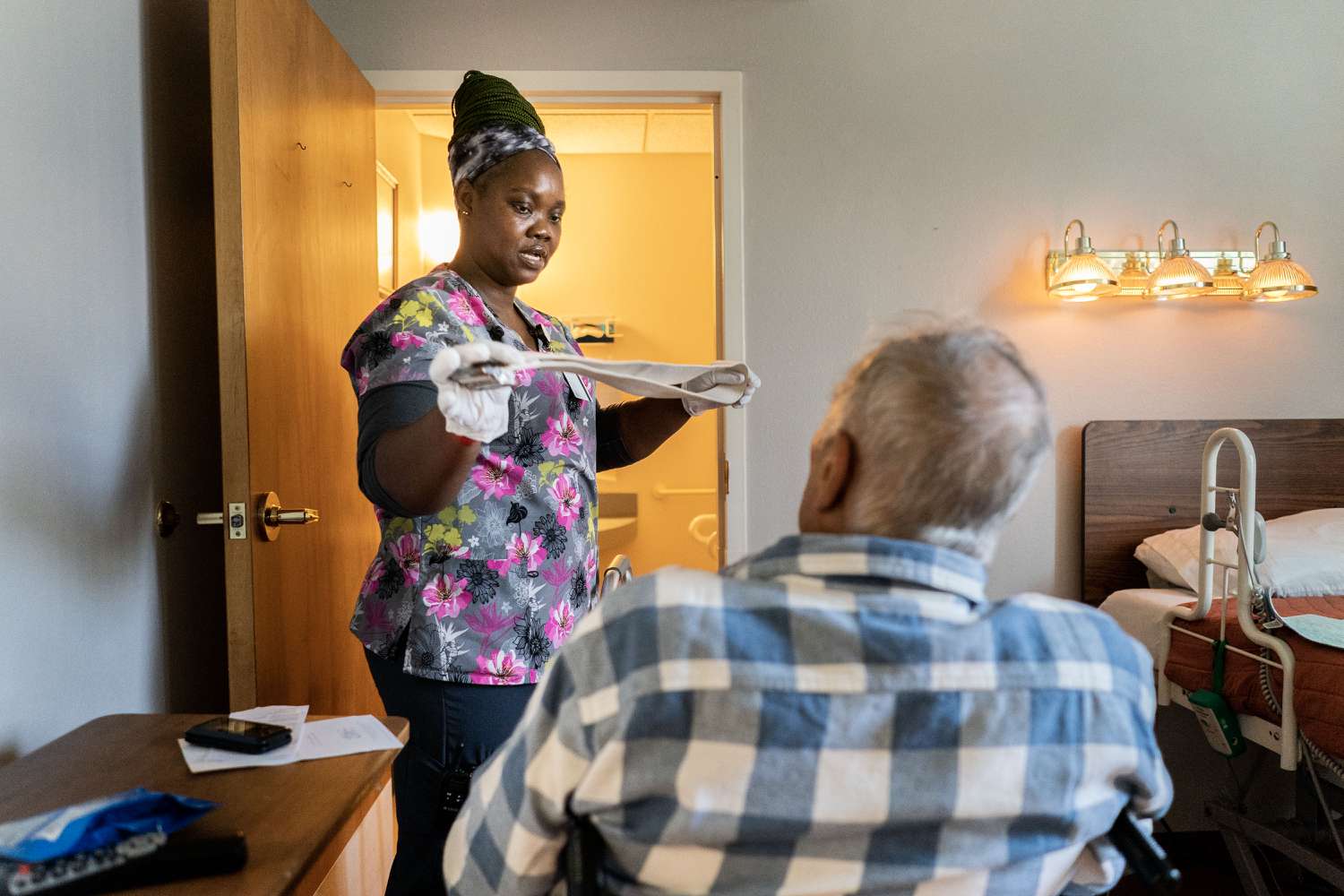 Caregiver assisting a seated elderly individual in a bedroom setting