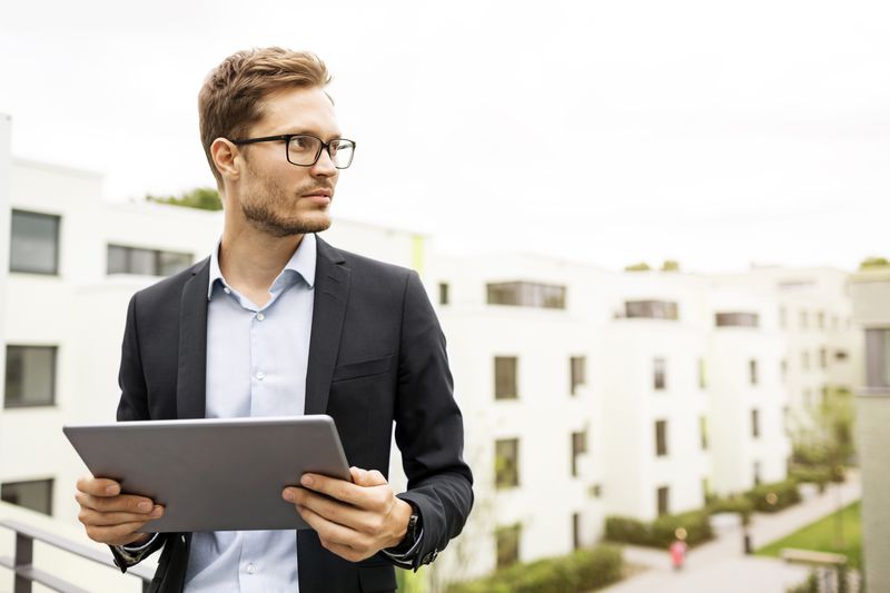 The manager of a real estate investment trust stands on the roof of an apartment building with other buildings in the apartment complex in the background behind them.