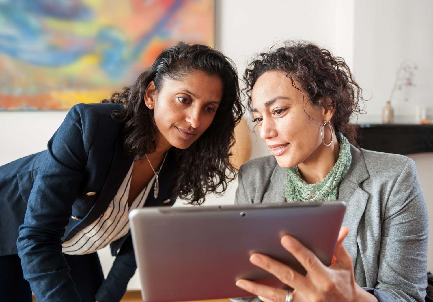 Two businesswomen looking at a tablet computer, discussing a topic.