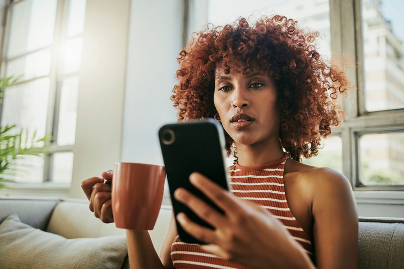 Black woman holding a coffee cup and reading on her phone