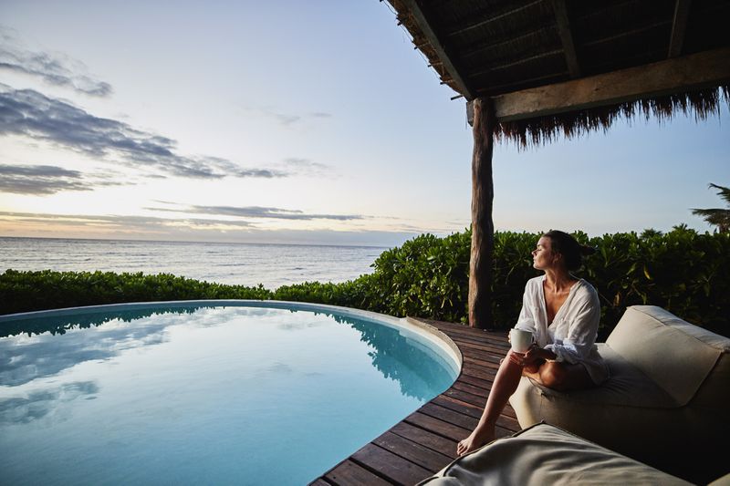 Wide shot of woman enjoying sunrise next to a pool overlooking the ocean