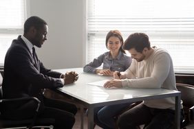 Two people meeting with a banker and signing paperwork