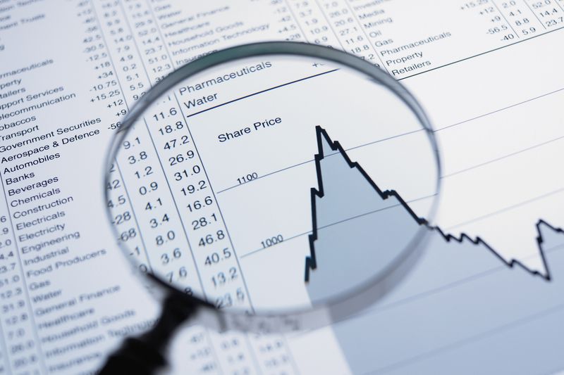 A magnifying glass and descending line graph and list of share prices.